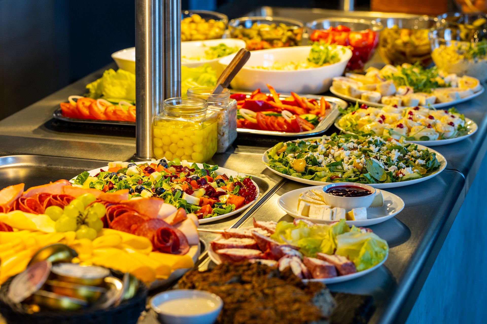 Bufet restauracyjny, zastawiony tzw. zimną płytą. Na talerzach i półmiskach wystawione warzywa, wędliny, wyroby garmażeryjne, pikle.