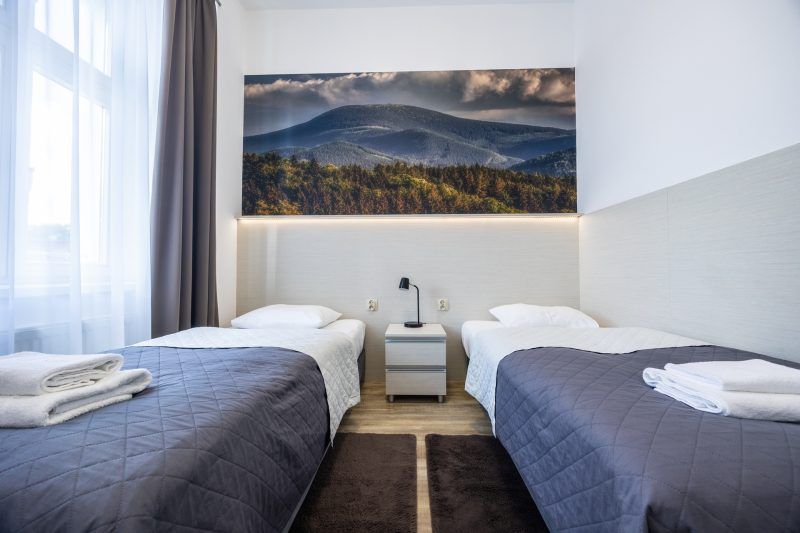 Pokój hotelowy z 2 pojedynczymi łóżkami. Na ścianie fototapeta z górskim krajobrazem.