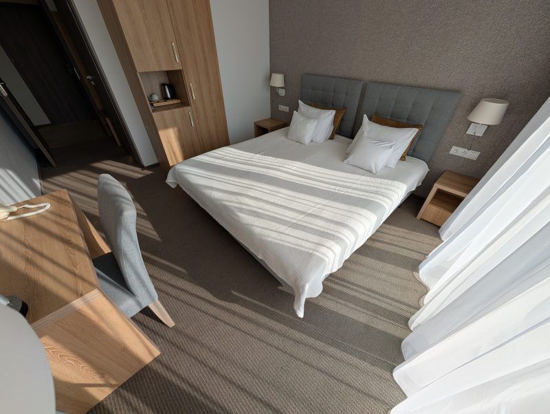 Pokój hotelowy z podwójnym łóżkiem z szafkami nicnymi oraz komodą z krzesłem