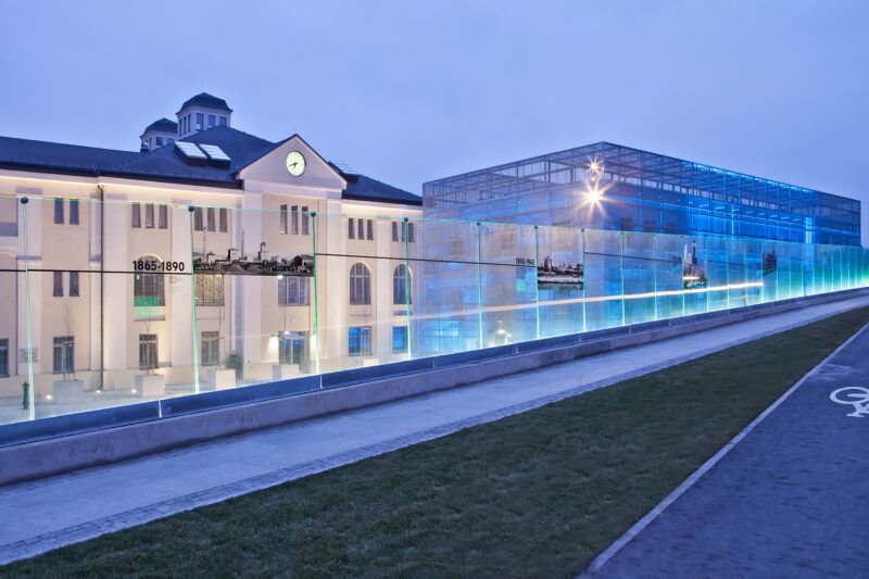 Widok na zrewitalizowaną część Starej Kopalni, do której przylega modernistyczny szklany budynek, oświetloną neonami.