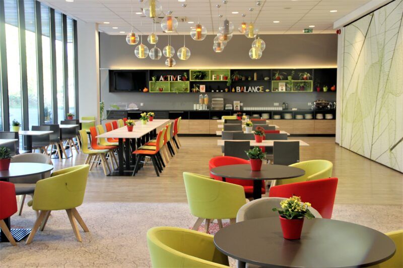Nowoczesna dobrze doświetlona restauracja z owalnymi stołami i kolorowymi fotelami.