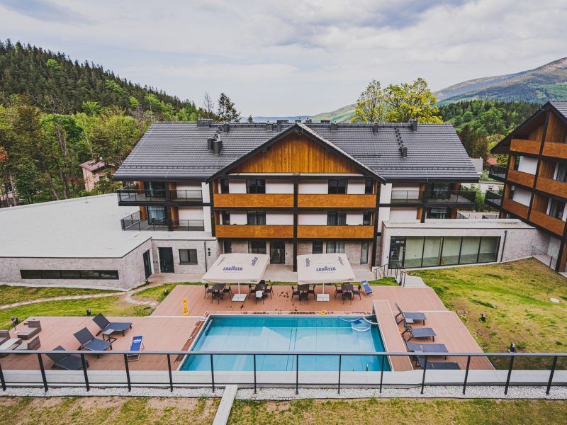 Widok na budynek hotelu z widocznym basem i z górami w tle