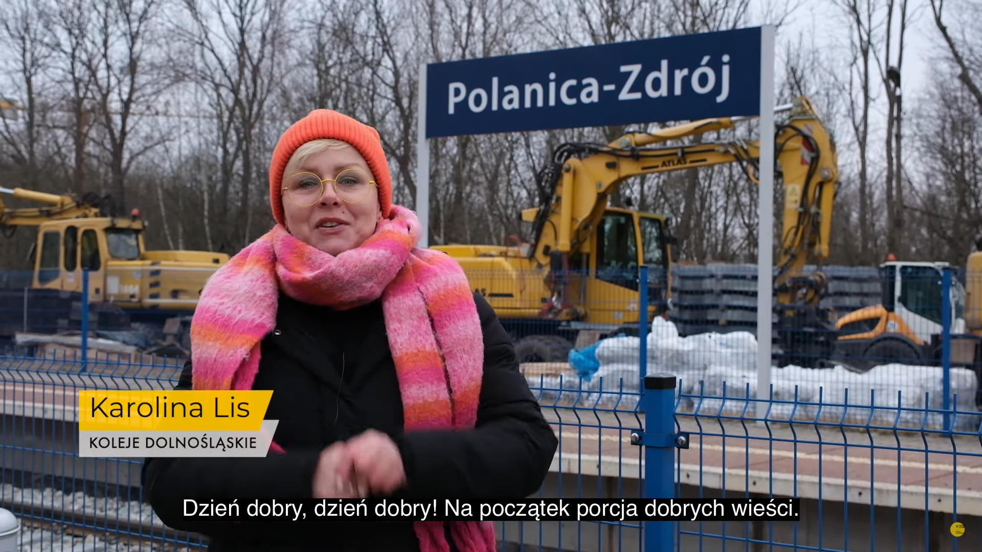 Kobieta w zimowym stroju stoi na peronie z widoczną tablicą Polanica-Zdrój
