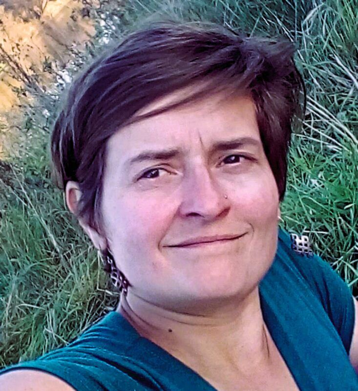 autoportret kobiety z średniej długości włosami, w niebieskiej koszulce, stojąca na tle zieleni