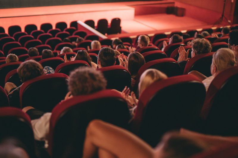 widok w sali kinowej z czerwonymi siedzeniami, wypełnionymi ludźmi