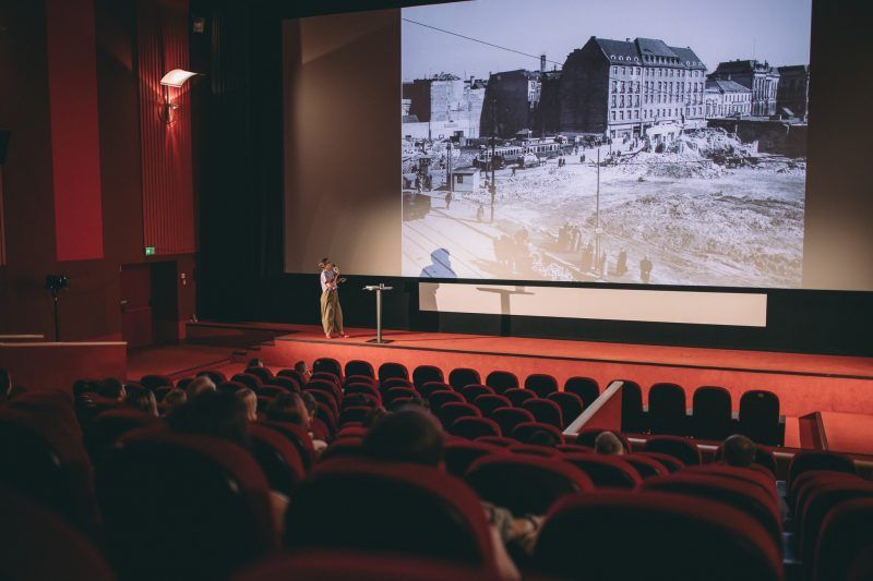 widok na całą sale kinową i kobietę prezentująca na scenie