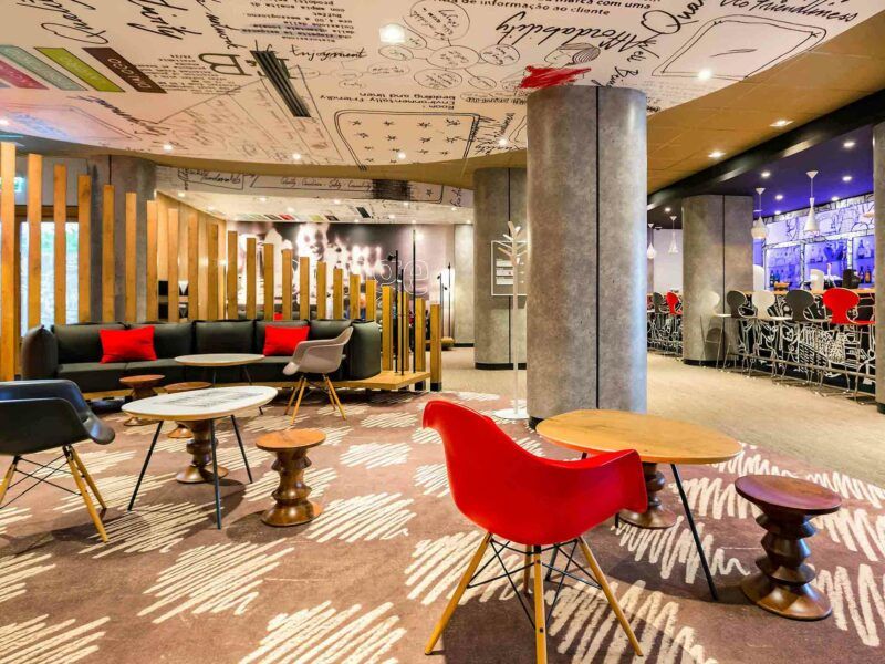 Lobby hotelowe w nowoczesnym modernistycznym stylu, z nowoczesnymi krzesłami oraz stolikami w nietuzinkowych kształtach. Na ścianie i suficie modernistyczna fototapeta.
