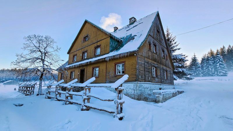 drewniane schronisko ukazane na zdjęciu od boku, pokryte śniegiem