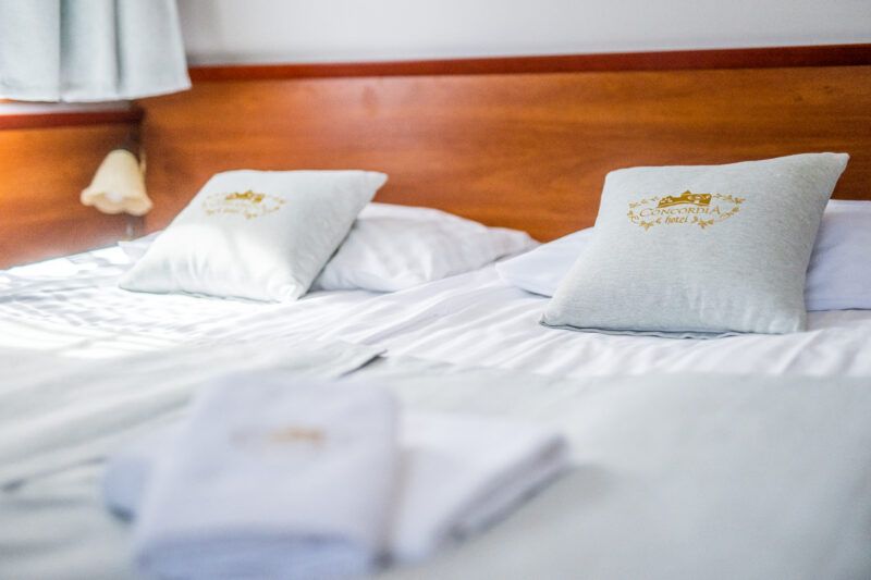 Łoże małżeńskie nakryte pościelą sygnowaną logo hotelu Concordia. 