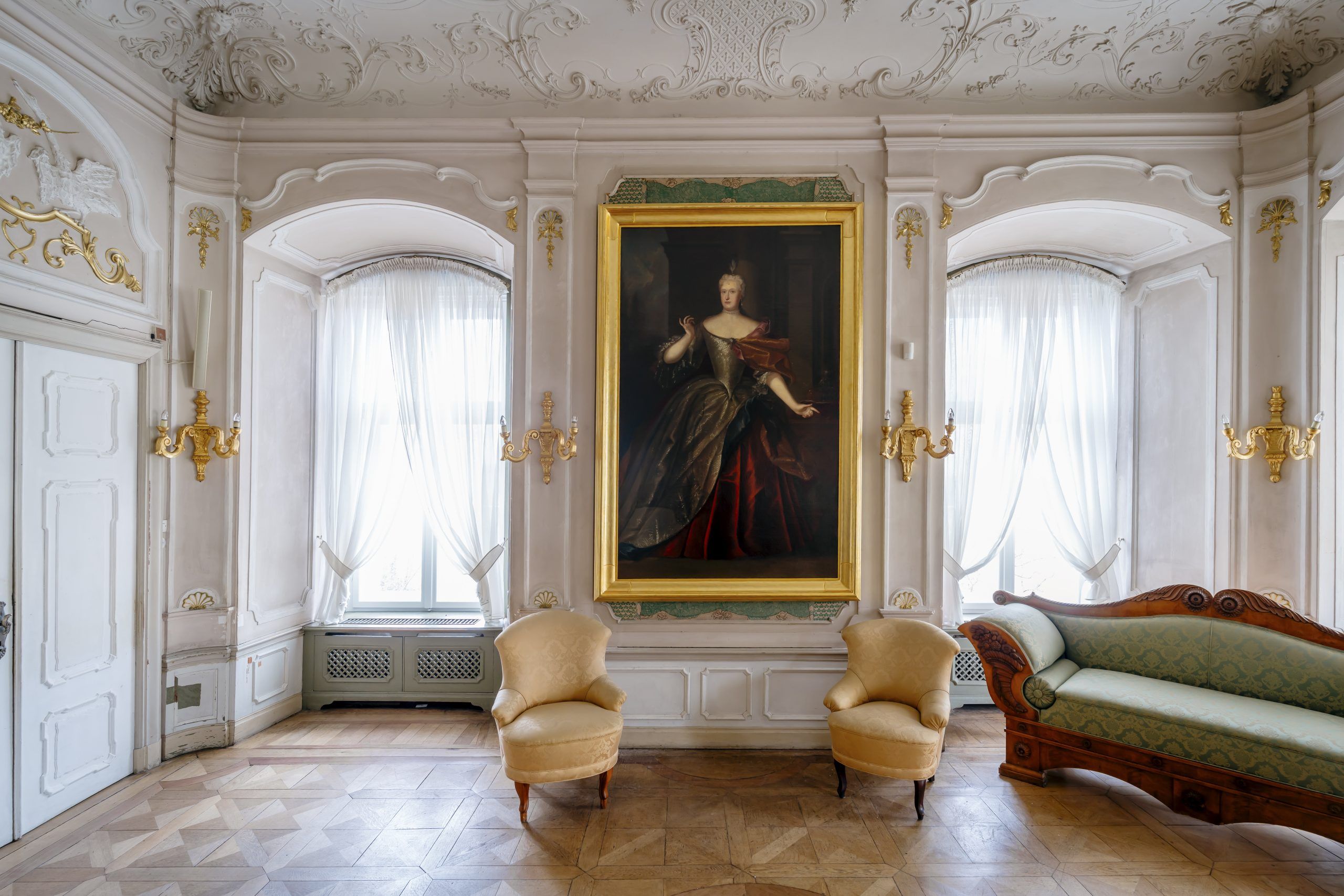 Zdjęcie przedstawia obraz z damą w pozłacanej ramie zawieszony w eleganckim wnętrzu z epoki