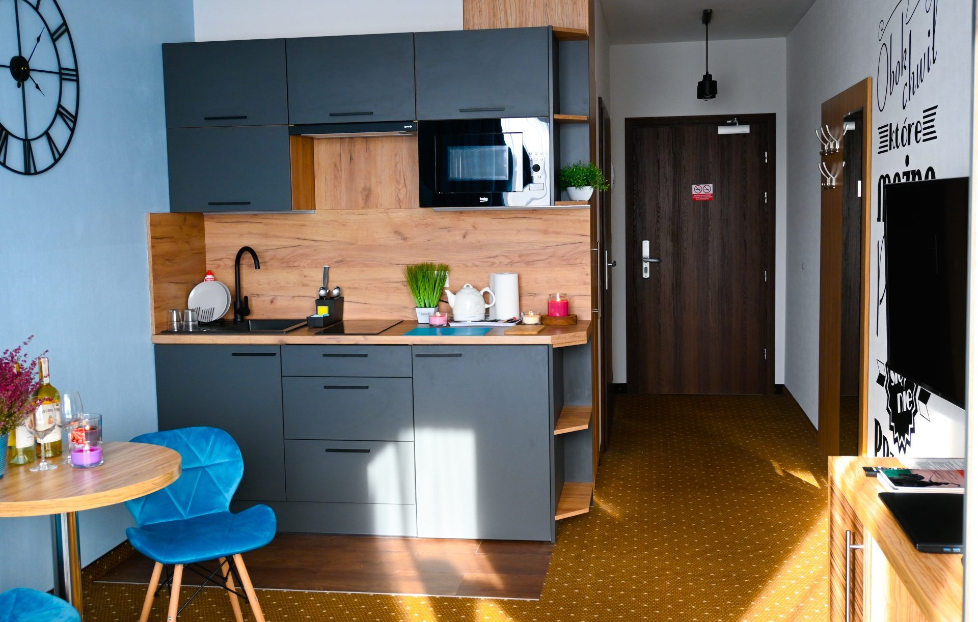 Przestronny, doświetlony apartament składający się z aneksu kuchennego i części wypoczynkowej pokoju z telewizorem.