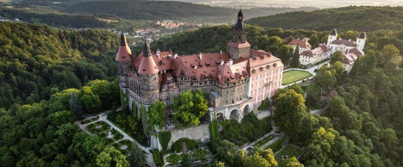 Zdjęcie z lotu ptaka na duży, stary zamek zbudowany na szczycie wzniesienia w otoczeniu przyrody