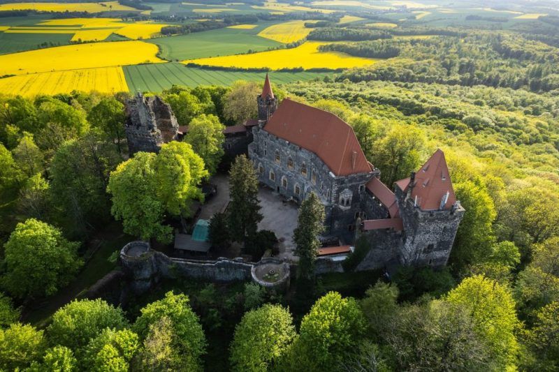 Zdjęcie przedstawia zamek widoczny z lotu ptaka z kwitnącym rzepakiem na polach w tle