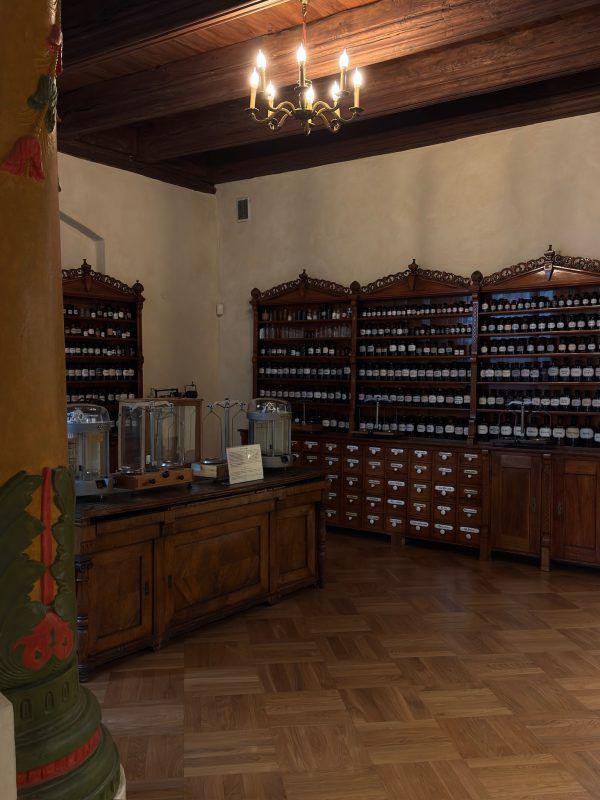 Zdjęcie przedstawia jedną z sal muzeum wyposażoną w stare drewniane komody wypełnione pojemnikami z lekami.