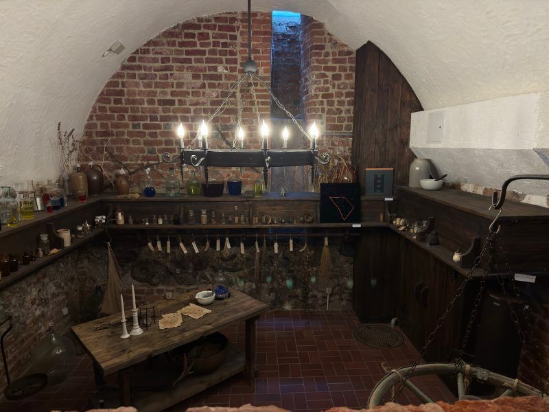 Obrazek przedstawia podziemną pracownię alchemiczną, która jest wypełniona, drewnianym i starym wyposażeniem znajduje się w muzeum farmacji.