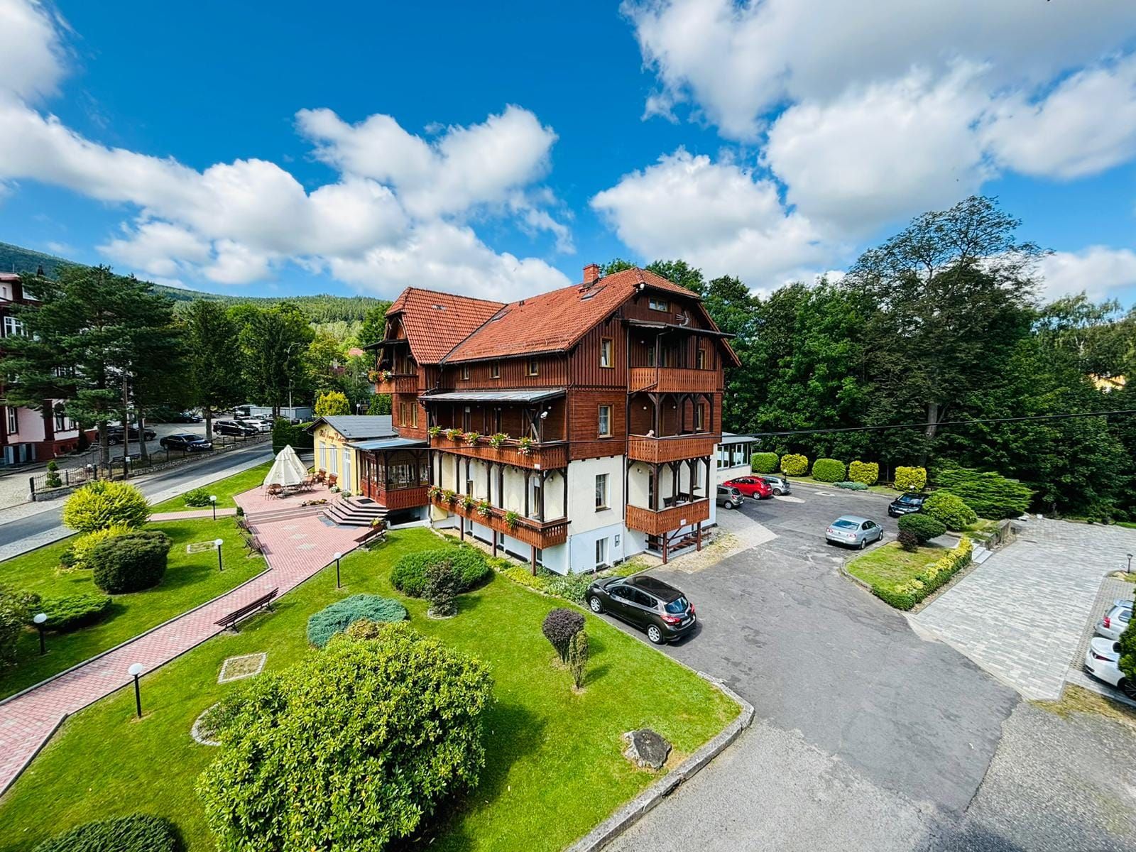 Elegancki budynek o klasycznej architekturze, otoczony zielenią. Jego jasna fasada i duże okna nadają mu przytulny, uzdrowiskowy charakter. Przy budynku duży parking. 