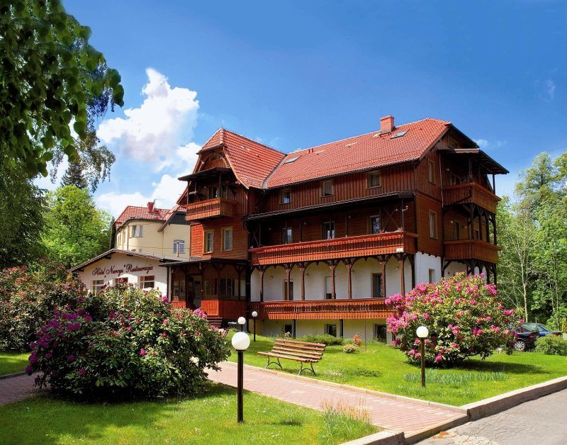 hotel w górskim otoczeniu, z pięknie zagospodarowanym terenem wokół. Widać zadbany ogród i wygodne miejsce do wypoczynku na świeżym powietrzu.