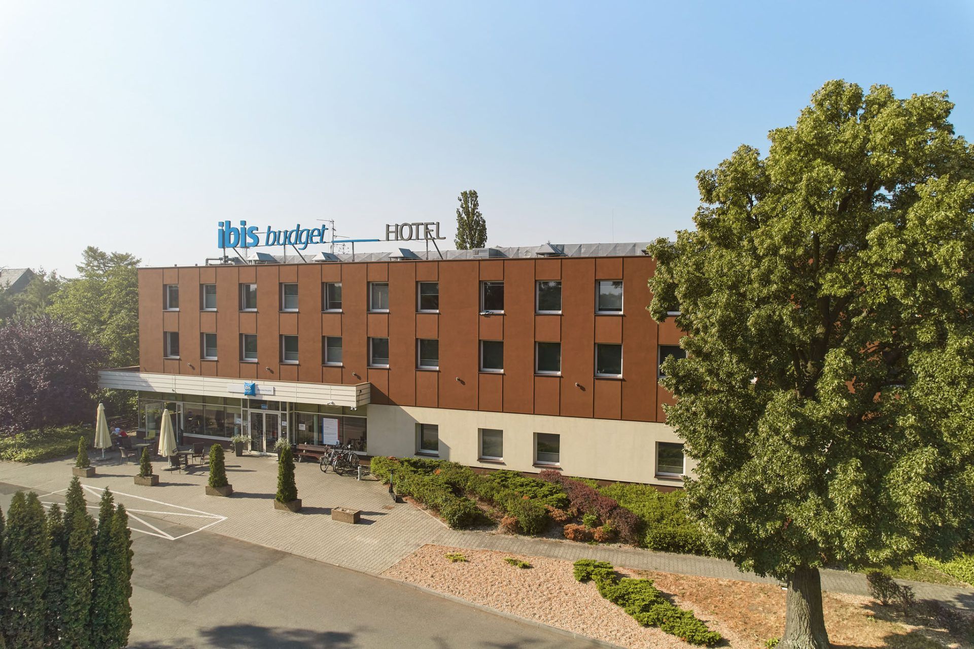 Długi nowoczesny budynek hotelowy w świetle promieni słonecznych w krajobrazie pełnym zieleni.
