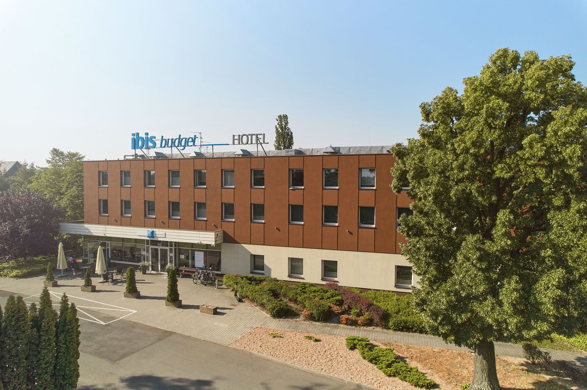 Długi nowoczesny budynek hotelowy w świetle promieni słonecznych w krajobrazie pełnym zieleni.
