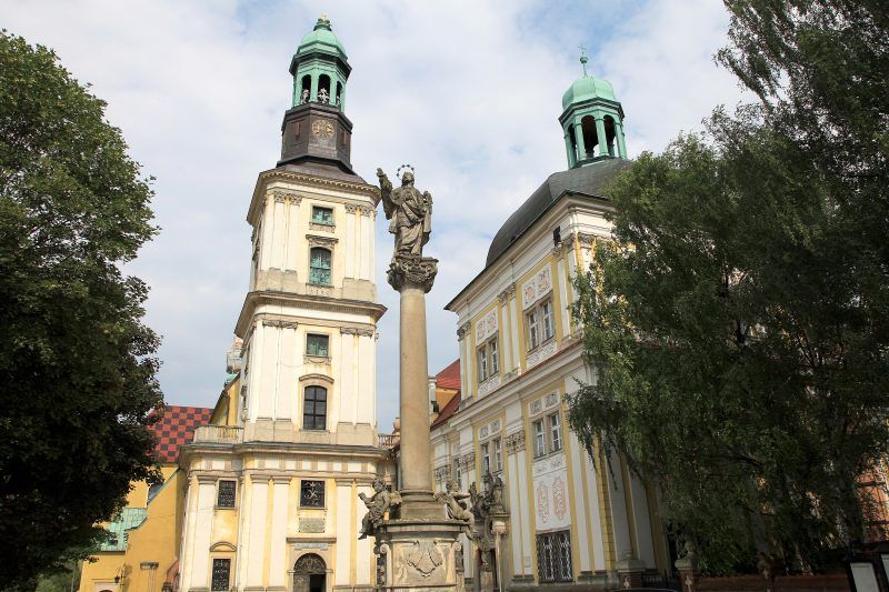 Zdjęcie przedstawia budynek klasztoru i kościoła z kolumną na pierwszym planie