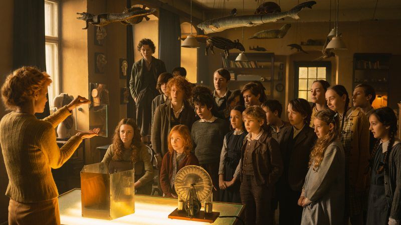 Kadr przedstawiający scenę z filmu Kajtek Czarodziej z grupą dzieci słuchających nauczycielki