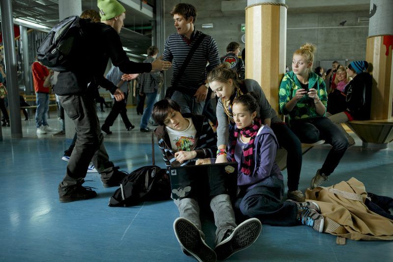 Kadr z filmu przedstawiający młodzież szkolną podczas przerwy spoglądającą na ekran laptopa
