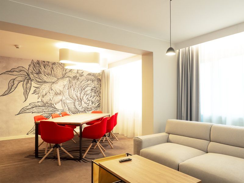 Część wypoczynkowa apartamentu typu suite. Kanapa ze ławą oraz stół z krzesłami. Na ścianie fototapeta z kwiatami. 