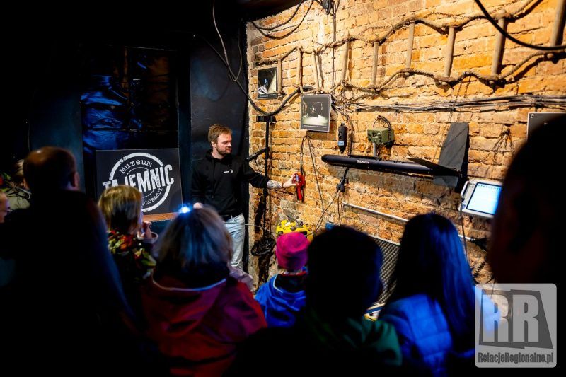 zdjęcie przedstawia mężczyzne wskazującego na eksponaty powieszone na ceglanej ścianie