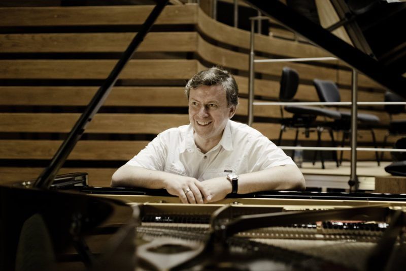 Mężczyzna siedzący za fortepianem na tle wnętrza filharmonii