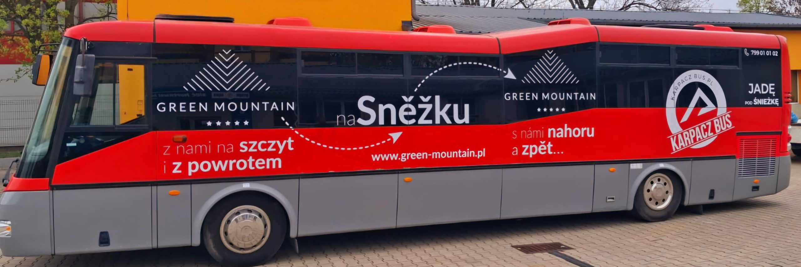 Zdjęcie przedstawia widok boczny na autobus turystyczny w kolorze czerwono-szarym