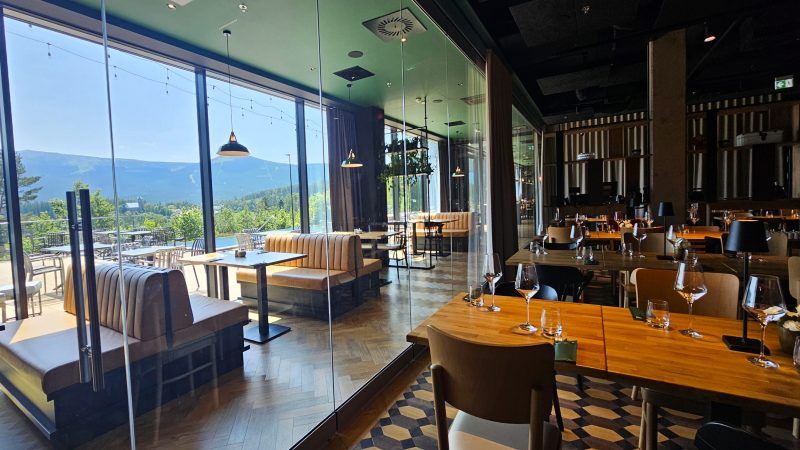 Duża, przestronna restauracja z drewniano-brązowym wystrrojem. Przestrzeń ogranicza duże okno wychodzące na taras skierowany w stronę gór. 