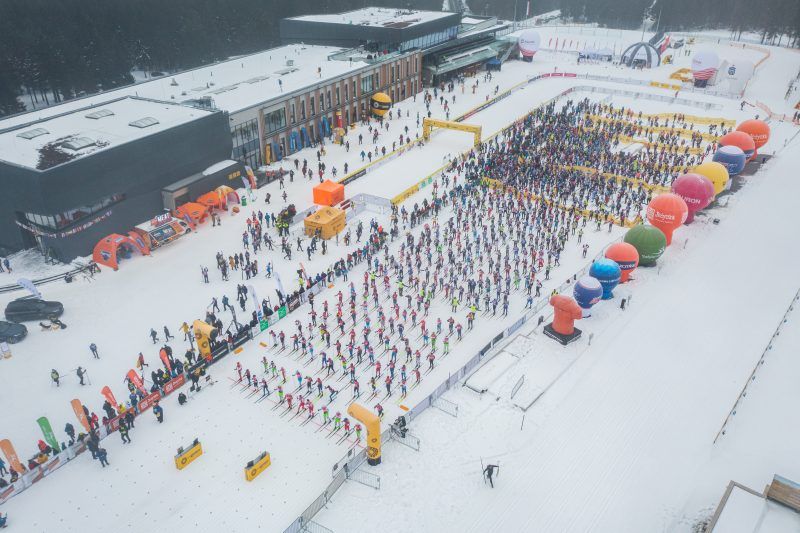 widok z drona na polanę zasypaną śniegiem i mnóstwo narciarzy startujących w biegu