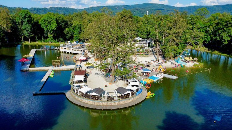 Zdjęcie wykonane z drona przedstawiajace cypel wypełniony zapleczem turystycznym na jeziorze w górach