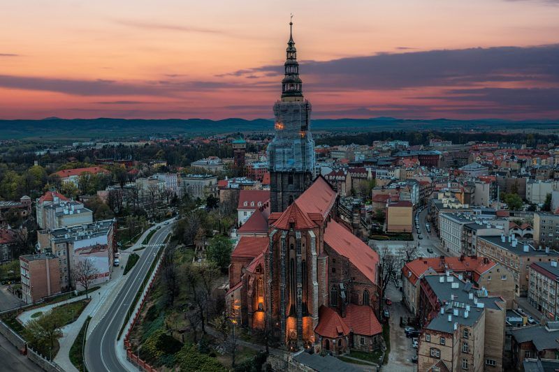Imponująca budowla z wysokimi, strzelistymi wieżami, których szczyty sięgają nieba, a na tle nieba wyróżnia się gotycka fasada, ozdobiona bogatymi detalami i witrażami, z majestatycznymi przyporami podpierającymi mur.