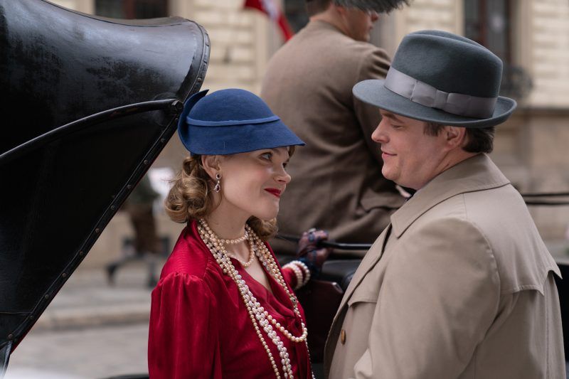 Mężczyzna i kobieta w strojach z lat 30 spoglądają na siebie uśmiechając się.