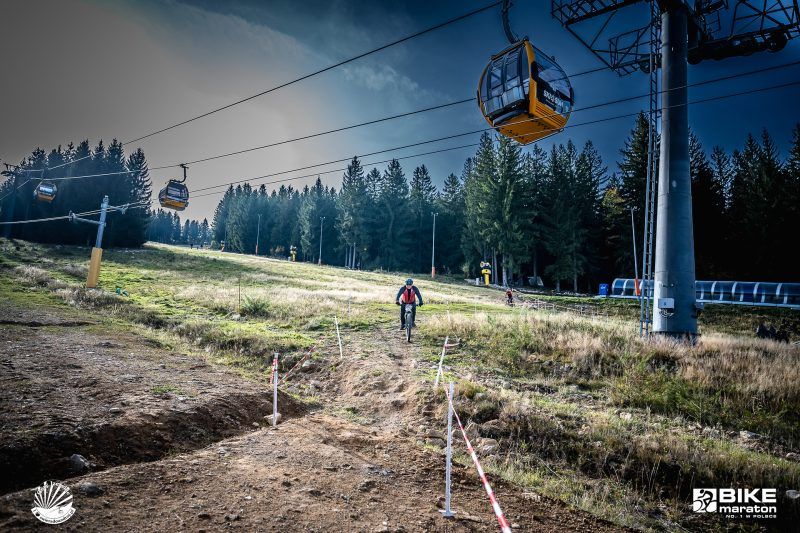 Zbocze po którym zjeżdża rowerzysta a nad nim po kolei gondolowej 